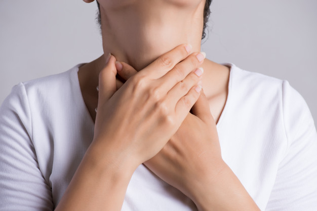 Seorang wanita berbaju putih sedang memegang tenggorokan dengan kedua tangannya karena nyeri karena mengalami gejala akalasia