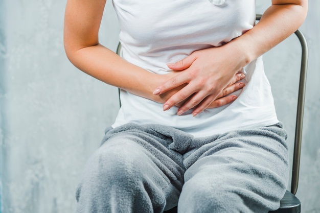 Seorang wanita duduk sambil memegang perutnya yang sakit karena gejala kolitis ulseratif
