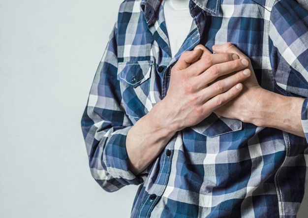 Seorang pria muda berbaju kotak-kotak sedang memegang dada dengan kedua tangannya karena gejala penyakit jantung bawaan
