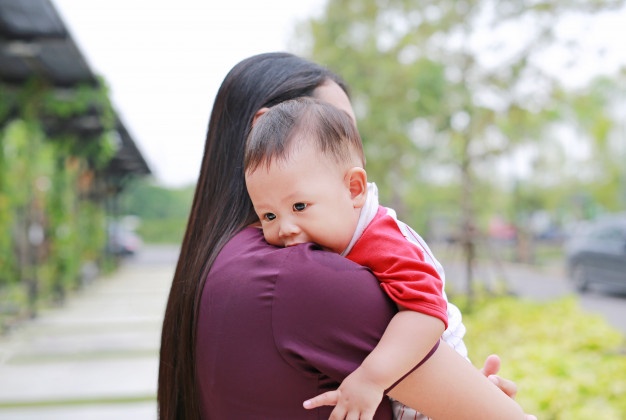 Seorang ibu menggendong bayi di sebuah taman